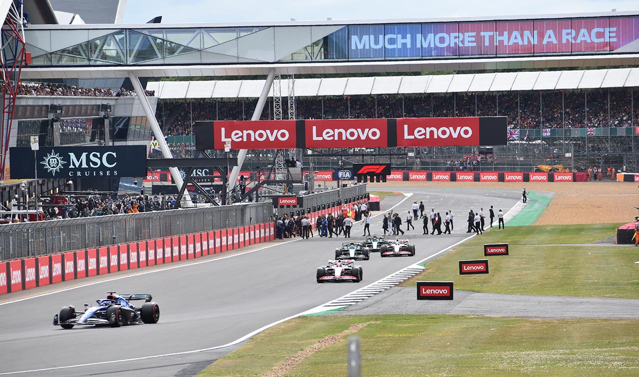 f1 cars racing past the start line at silverstone, with grandstands in the background