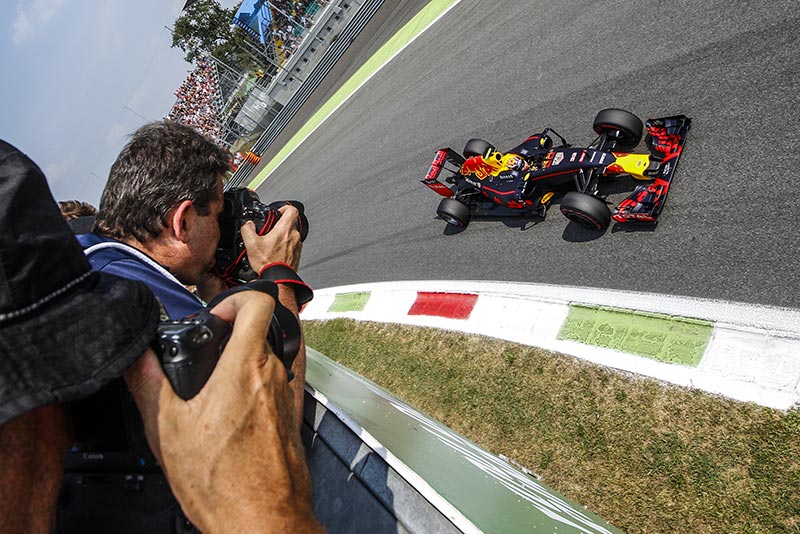 photographer taking a picture of a red bull f1 racing car zooming past