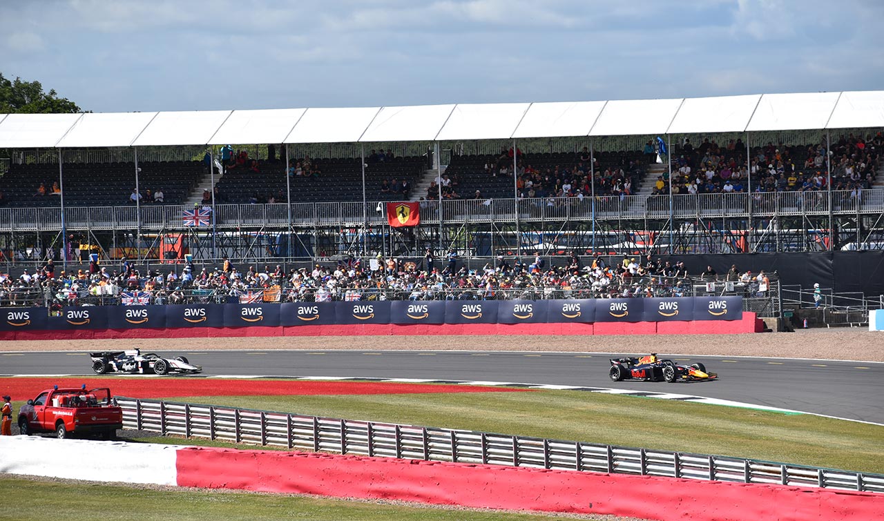 2 f2 cars racing with grandstand in view with ferrari flag
