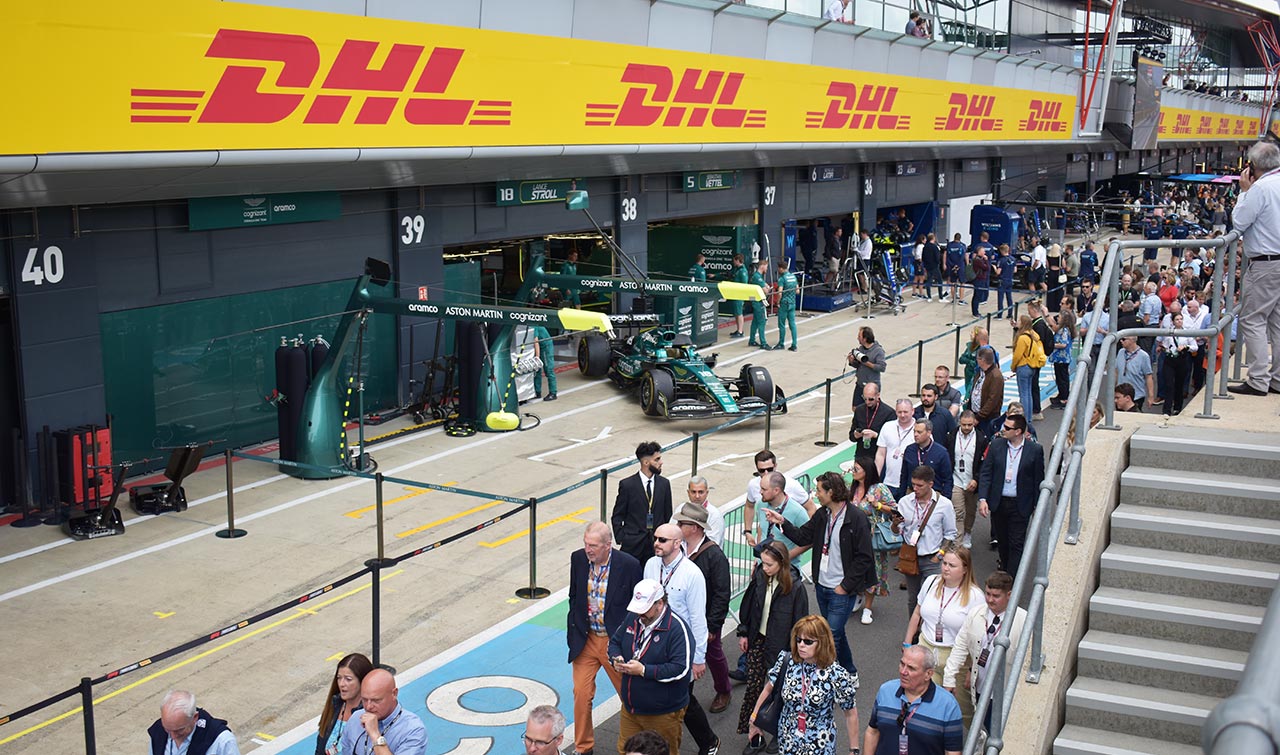 pitlane with fans going by, DHL signs and a aston martin in the background