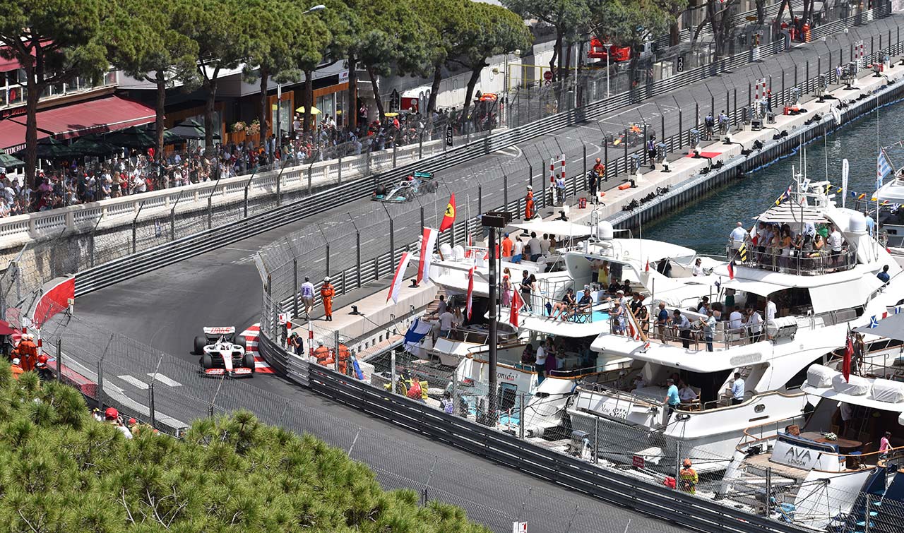2 F1 cars racing round a car with fans viewing from luxury yachts