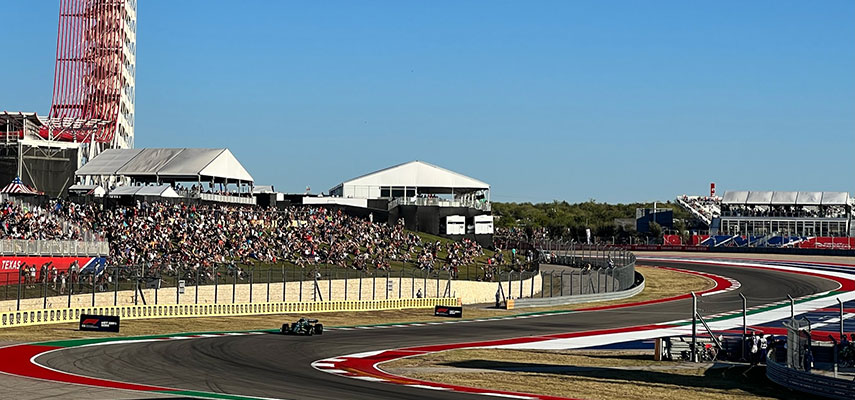 f1 car approaching and the blue and white track with crowd in view