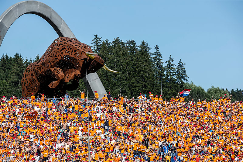 large crowd in orange at the austrian grand prix with a metal bull in the background