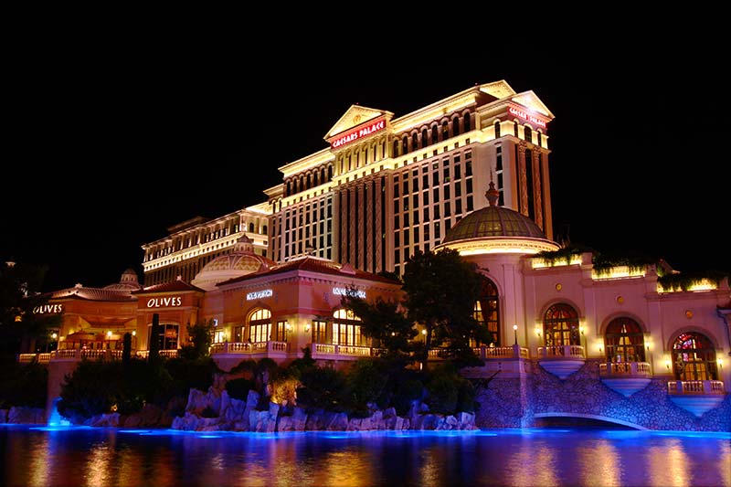 caesars palace hotel all lit up at night with restaurant and water pond in the front