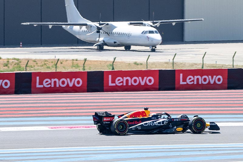 red bull max verstappen out in front with his f1 car with a plane in the background
