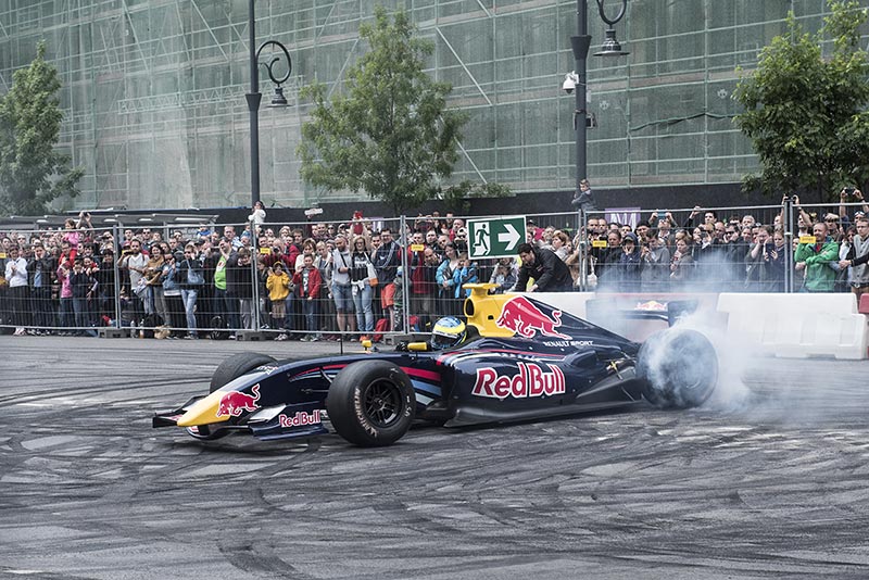 red bull f1 car screeching brakes with smoke and the crowd watching