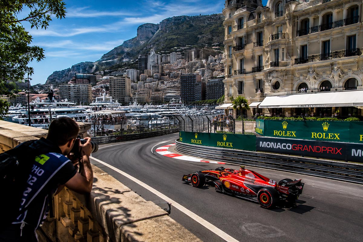 Photographer capturing a Formula 1 car racing at the Monaco Grand Prix with Monte Carlo and Port Hercule in the background